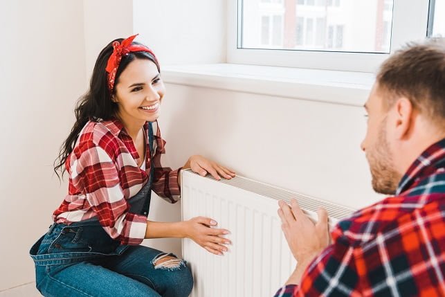 selective fcous of happy woman touching heating radiator while looking at boyfriend at home